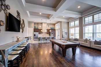 A billiard table is in the middle of a room with a bar and a television.